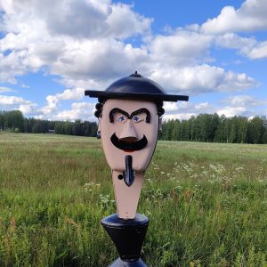 Vesa Väänäsen mustahattuinen pääfiguuri heinäpeltomaisemassa